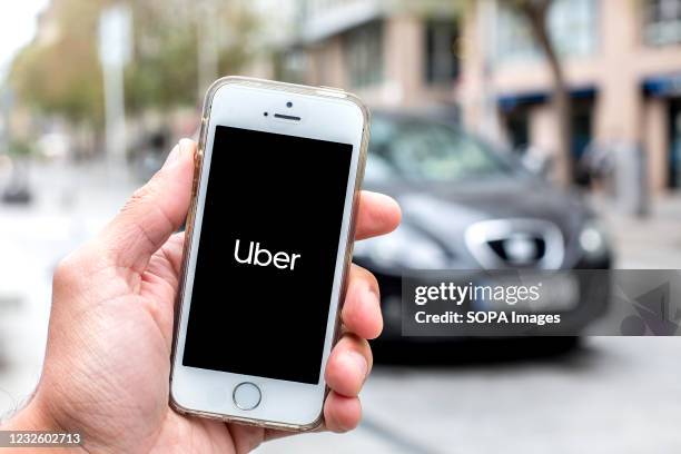 In this photo illustration a Uber logo seen displayed on a smartphone screen with a car in the background.