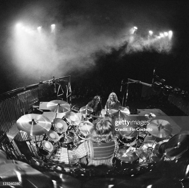 View looking from the back of the stage, looking out over drummer Neil Peart sitting at his drumkit with guitarist Alex Lifeson and bassist Geddy Lee...