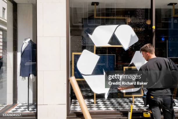 Male retaill contractor pastes a recyclig sticker on to the window surface at the Jermyn Street branch of Charles Tyrwhitt, on 27th April 2021, in...