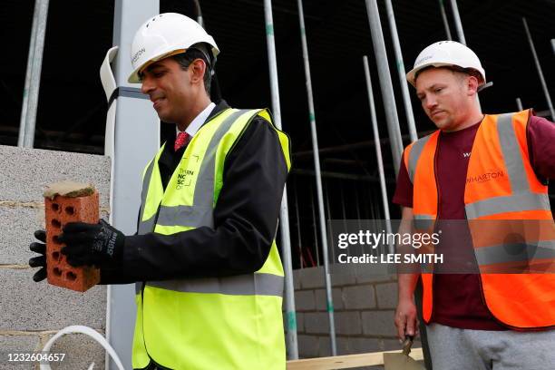 Britain's Chancellor of the Exchequer Rishi Sunak , wearing a hard hat and a hi-vis jacket, holds a brick as he stands next to bricklayer Danny...