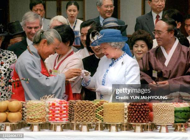 Queen Elizabeth II of Britain toasts with a South Korean dancer in front of the 73rd birthday party table during a visit to Hahoe Village near Andong...