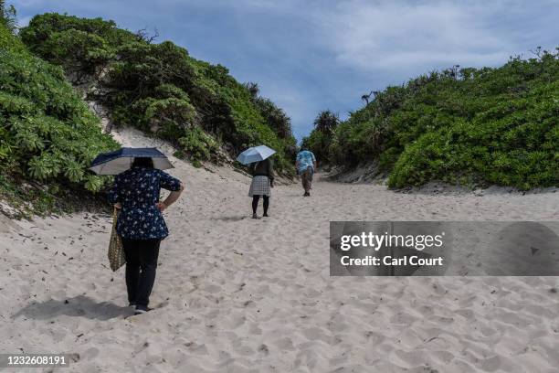 People shelter from the sun under umbrellas as they climb a sand dune after visiting a nearly empty beach on April 30, 2021 in Miyakojima, Japan....