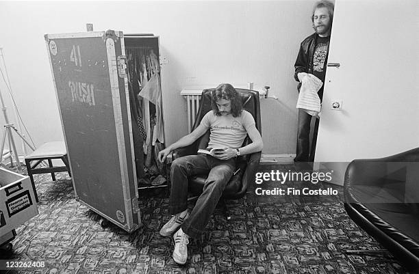 Neil Peart, drummer with Canadian rock band Rush, sitting backstage in armchair, reading a book beside a travel wardrobe with the door ajar, at the...