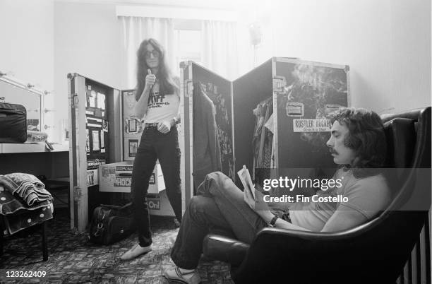 Geddy Lee, singer and bassist, and Neil Peart, drummer, of Canadian rock band Rush, pictured backstage with Peart sitting in an armchair, reading a...