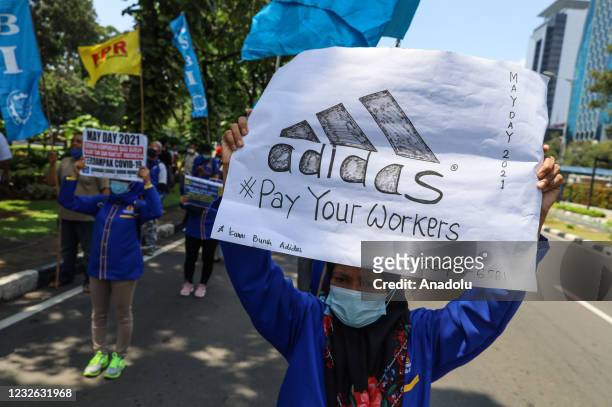An Indonesian worker carries an adidas poster during the International Workers' Day near the National Monument in Jakarta, Indonesia on May 1, 2021....