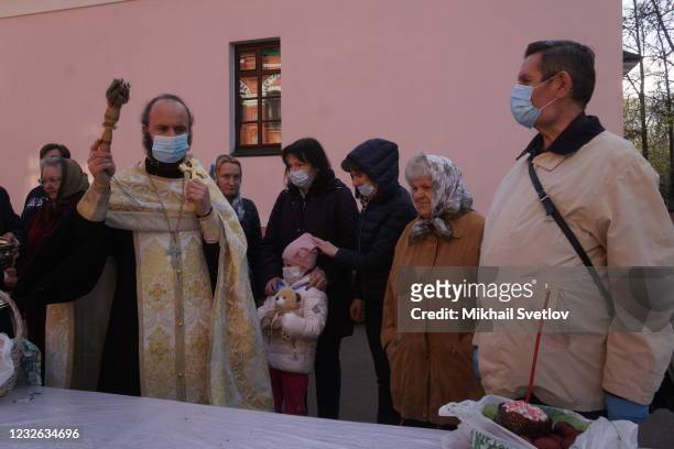 Russian Orthodox Church priest wearing a face mask to protect against the coronavirus blesses painted eggs and cakes prepared for the Orthodox Easter...