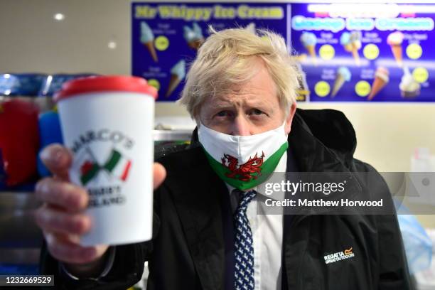 Prime Minister Boris Johnson wears a Welsh flag face mask and holds up a paper cup as he visits Marco’s cafe in Barry Island during the Senedd...