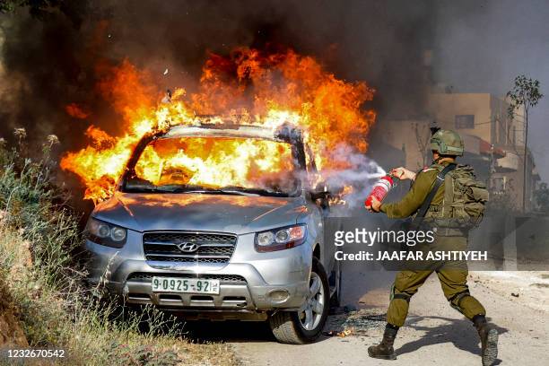 An Israeli soldier tries to extinguish flames in a burning Palestinian vehicle during a security operation in the village of Aqraba, east of Nablus...