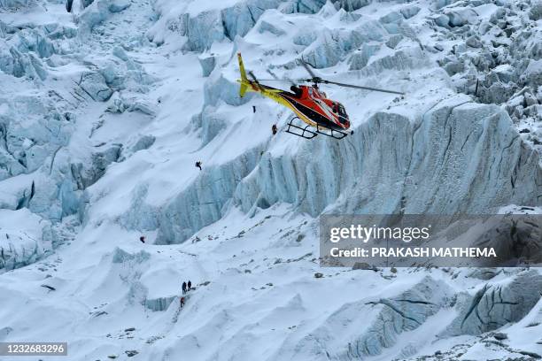 In this photograph taken on May 4, 2021 mountaineers trek along Khumbu glacier as an helicopter flies near the Everest base camp in the Mount Everest...