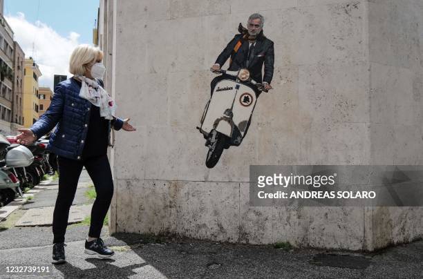 Woman walks past a mural by artist Harry Greb depicting the new coach of the AS Roma football team, Jose Mourinho riding a scooter bike, on a wall of...