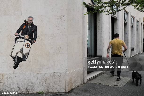 Man walks his dog past a mural by artist Harry Greb depicting the new coach of the AS Roma football team, Jose Mourinho riding a scooter bike, on a...