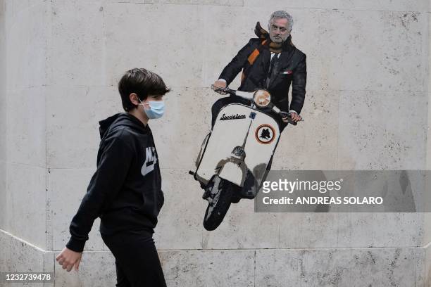 Boy walks past a mural by artist Harry Greb depicting the new coach of the AS Roma football team, Jose Mourinho riding a scooter bike, on a wall of a...