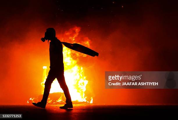 Palestinian protester walks by a burning tyre amid clashes with Israeli security forces at the Hawara checkpoint, south of Nablus city, in the...