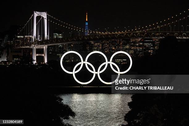 General view shows the Olympic rings lit up at dusk, with the Rainbow bridge and the Tokyo Tower in the background, on the Odaiba waterfront in Tokyo...