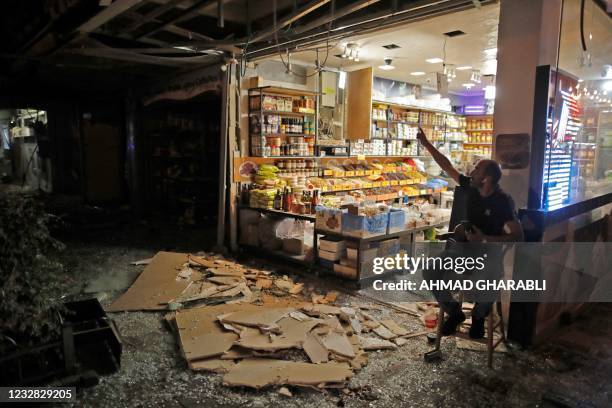 Shop keeper sits outside a store whose facade was damaged in Holon near Tel Aviv, on May 11 after rockets were launched towards Israel from the Gaza...