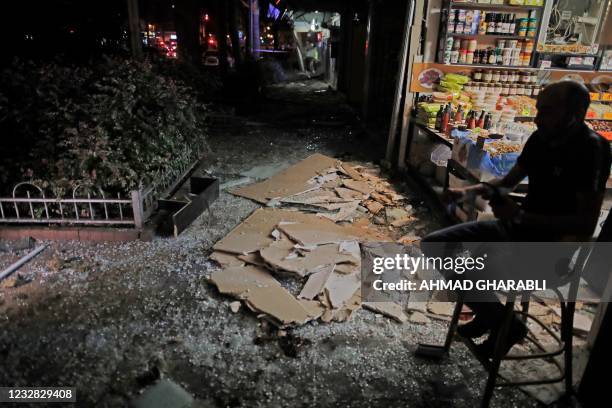 Shop keeper sits outside a store whose facade was damaged in Holon near Tel Aviv, on May 11 after rockets were launched towards Israel from the Gaza...