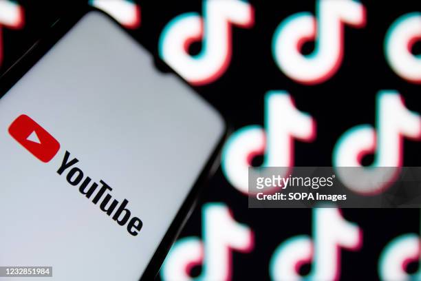 In this photo illustration a YouTube logo seen displayed on a smartphone screen with TikTok logos in the background. YouTube will pay $100 million to...