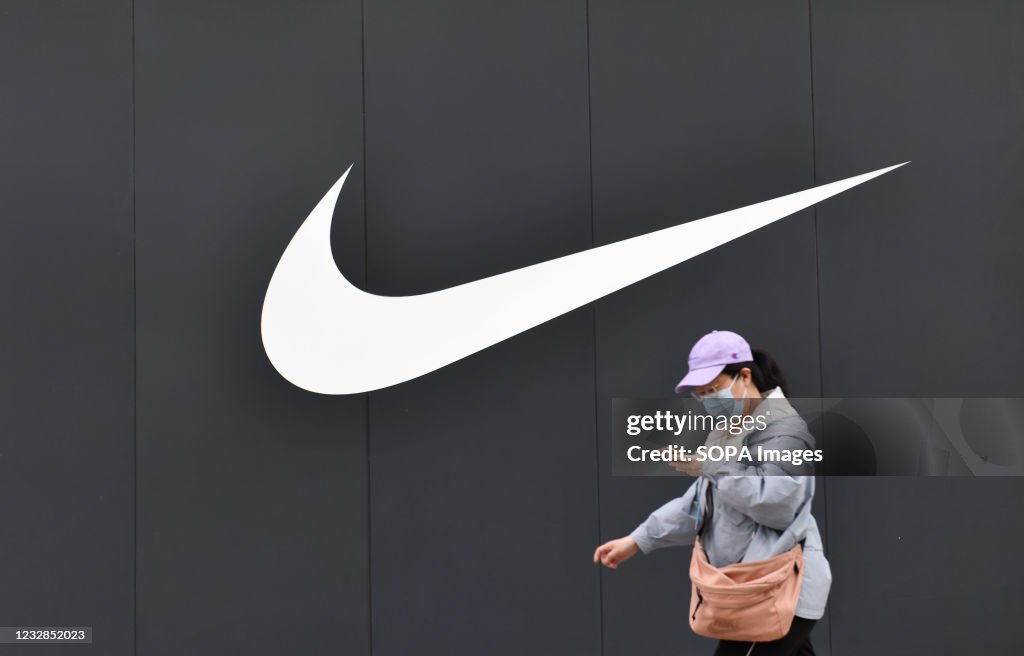 A woman wearing a facemask walks past a Nike logo and store...