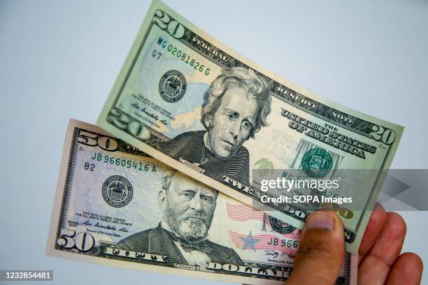 In this photo illustration, a person holds a collection of twenty and fifty Dollar banknotes.