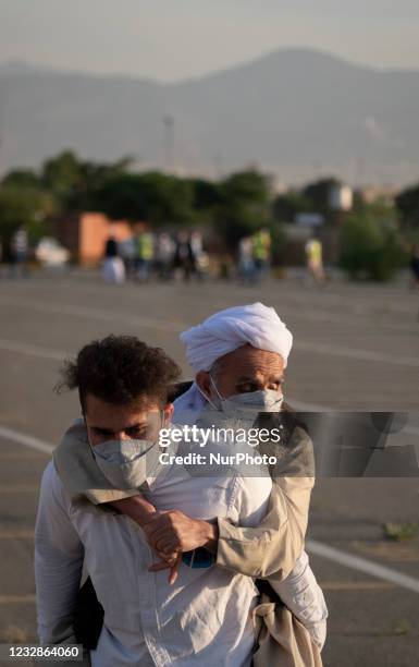 An Afghan Sunni refugee man carrying his elderly father while arriving an area that has used as a place for Eid al-Fitr mass prayer ceremonies...