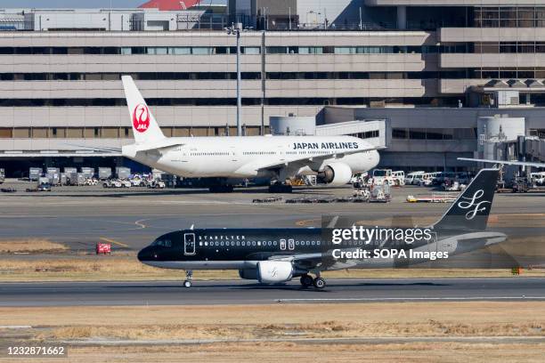 Airbus A320-214 airliner with Starflyer airlines passes in front of a JAL Boeing 777 at Haneda International Airport.