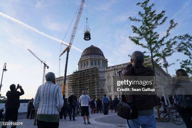 People watch as a crane lifts the newly-finished gold-covered cupola and cross onto the dome of the rebuilt Berlin City Palace on May 29, 2020 in...