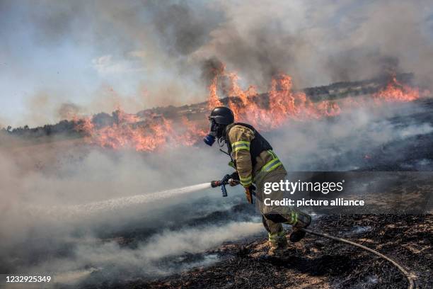 May 2021, Israel, Ashkelon: An Israeli firefighter battles a blaze in a field caused by a rocket fired from Gaza Strip towards Israel, amid the...