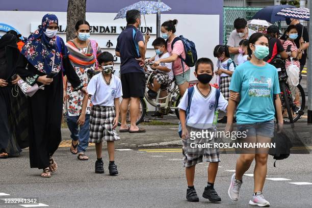 Children walk home with their guardians after school in Singapore on May 17 as the country prepares to shut all schools and switch to home-based...