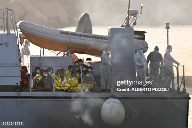 Migrants warmed by emergency blankets arrive on a boat of the Italian Guardia Di Finanza law enforcement agency on May 17, 2021 to disembark on the...