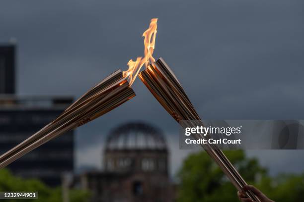 The atomic bomb dome stands in the background as Tokyo 2020 Olympic torch bearers exchange the flame during the torch relay in the Hiroshima Peace...