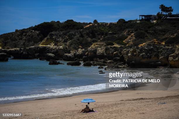 Woman sits under a beach umbrella at Oura beach, Albufeira, in Algarve, south of Portugal, on May 17, 2021. - British holidaymakers returned to...