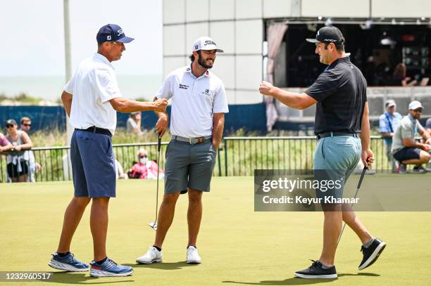 Max Homa and his temporary caddie Jim Bones Mackay greet Jon Rahm of Spain on the putting green during practice for the PGA Championship on The Ocean...