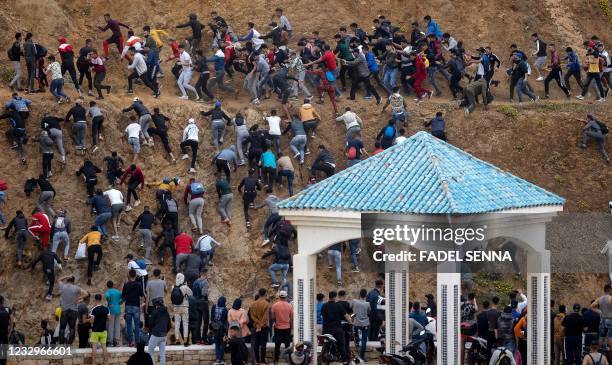 Migrants avoid the Moroccan police as they try to reach the border between Morocco and thr Spanish enclave of Ceuta on May 18, 2021 in Fnideq. - At...