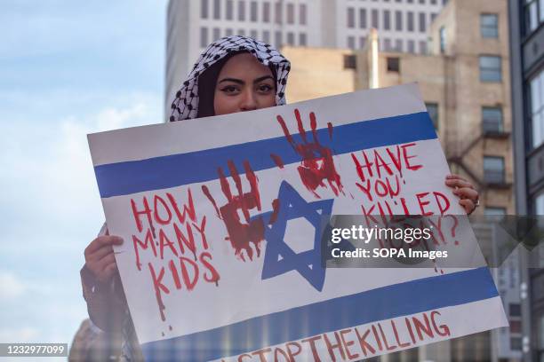 Protester sits on top of a car while holding a sign painted like the Israeli flag pointing out the deaths caused by Israel over the past few days....