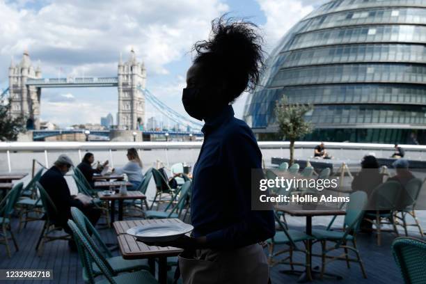 Waitress carries a plate in view of Tower Bridge at Tavolino Bar & Kitchen on May 19, 2021 in London, England. Although indoor drinking and dining...