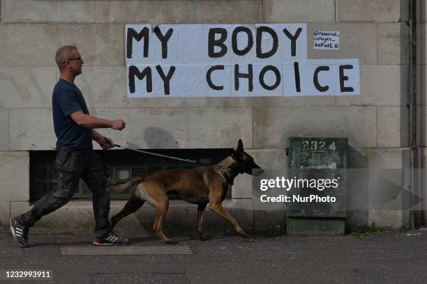 Man with a dog walks by 'My Body My CHoice' stickers seen on a wall in Belfast city center. On Wednesday, May 19 in Belfast, Northern Ireland