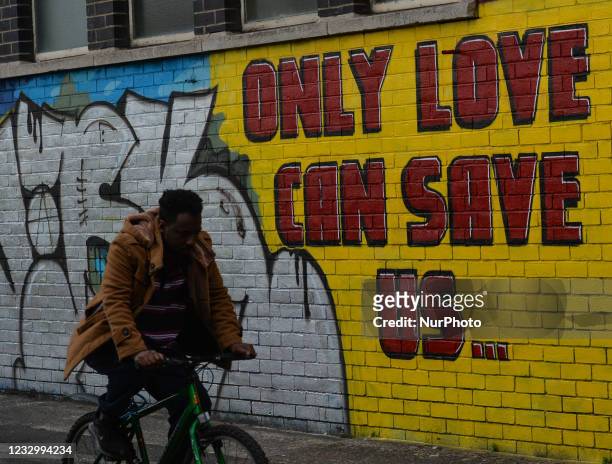 Man cycles by a mural with words 'Only Love Can Save Us...' seen in Belfast city center. On Wednesday, May 19 in Belfast, Northern Ireland