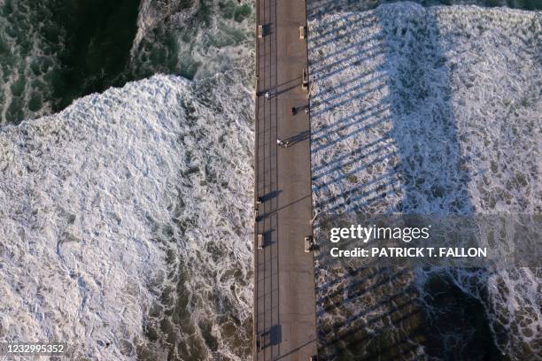 In this aerial image, people walk on the Huntington Beach pier before sunset on May 19, 2021 in Huntington Beach, California. - Orange County is now...
