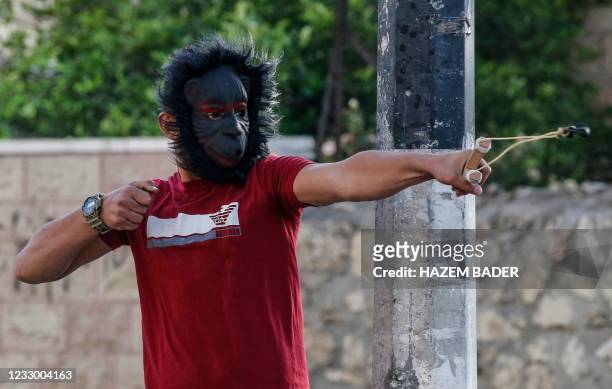 Palestinian demonstrator wearing a Gorilla mask uses a slingshot to hurl stones during confrontations with Israeli troops in the occupied West Bank...