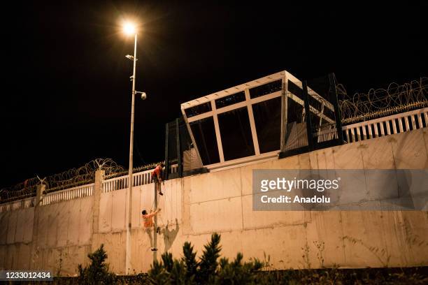 Migrant climbs the border wall by throwing a rope with the help of another migrant in Spanish enclave of Ceuta on May 21, 2021. Eight thousand...