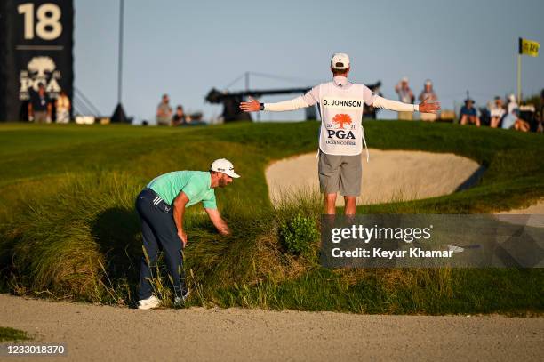 Dustin Johnson searches for his ball in the tall grass as his brother measures the distance for a penalty drop off the green on the 18th hole during...