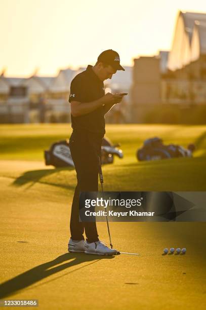 Jordan Spieth checks his phone as he practices putting at sunset on the practice green during the first round of the PGA Championship on The Ocean...