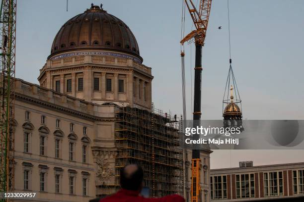 Man watches as a crane lifts the newly-finished gold-covered cupola and cross onto the dome of the rebuilt Berlin City Palace on May 29, 2020 in...