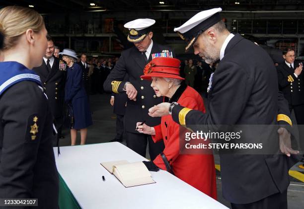 Britain's Queen Elizabeth II signs the visitors' book as is greeted by Commanding Officer Captain Angus Essenhigh and Commodore Stephen Moorhouse,...