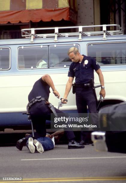 An African-American man lying on the ground while being handcuffed at gunpoint during his arrest by white Los Angeles police officers in Hollywood,...