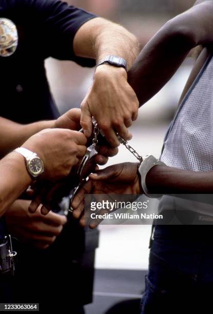 An African-American man is put in handcuffs after being arrested at gunpoint by white Los Angeles police officers in Hollywood, California, circa...