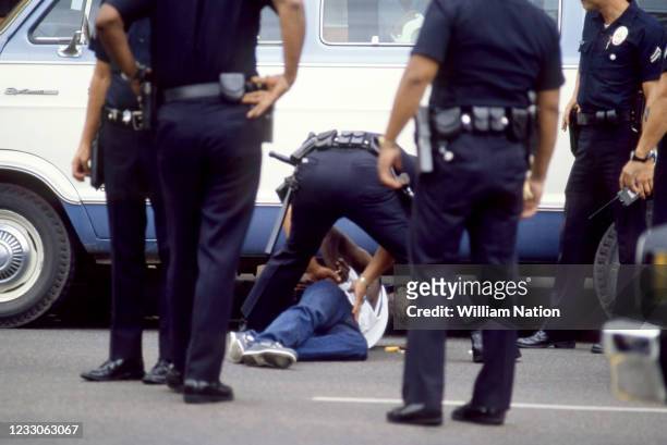 An African-American man lying on the ground while being handcuffed at gunpoint during his arrest by white Los Angeles police officers in Hollywood,...