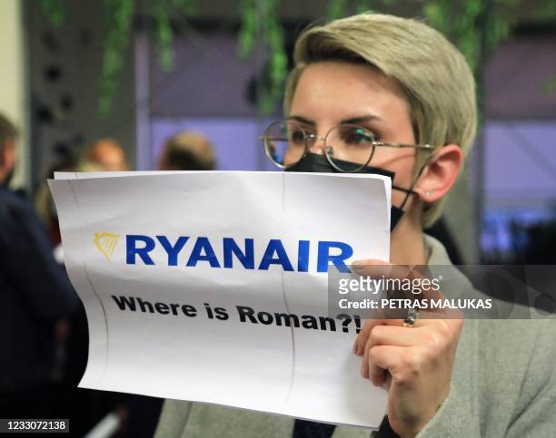 Woman stands with a poster reading 'Where is Roman ?!' in the arrival area as passengers disembark from a Ryanair passenger plane from Athens,...