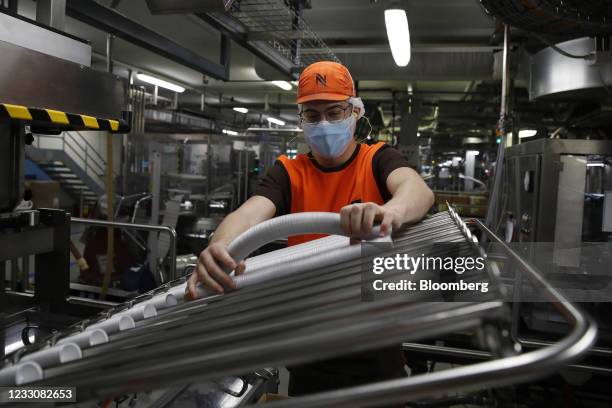 An employee wearing a protective face mask loads capsule packaging into a machine on the production line at Nestle SA's Nespresso plant in Avenches,...