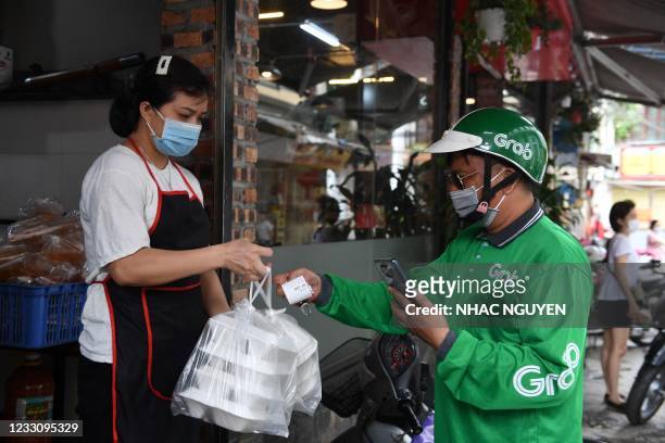 Grab delivery service personnel receives a take away food order from an eatery staff in Hanoi on May 25, 2021 as city authorities expanded closure...